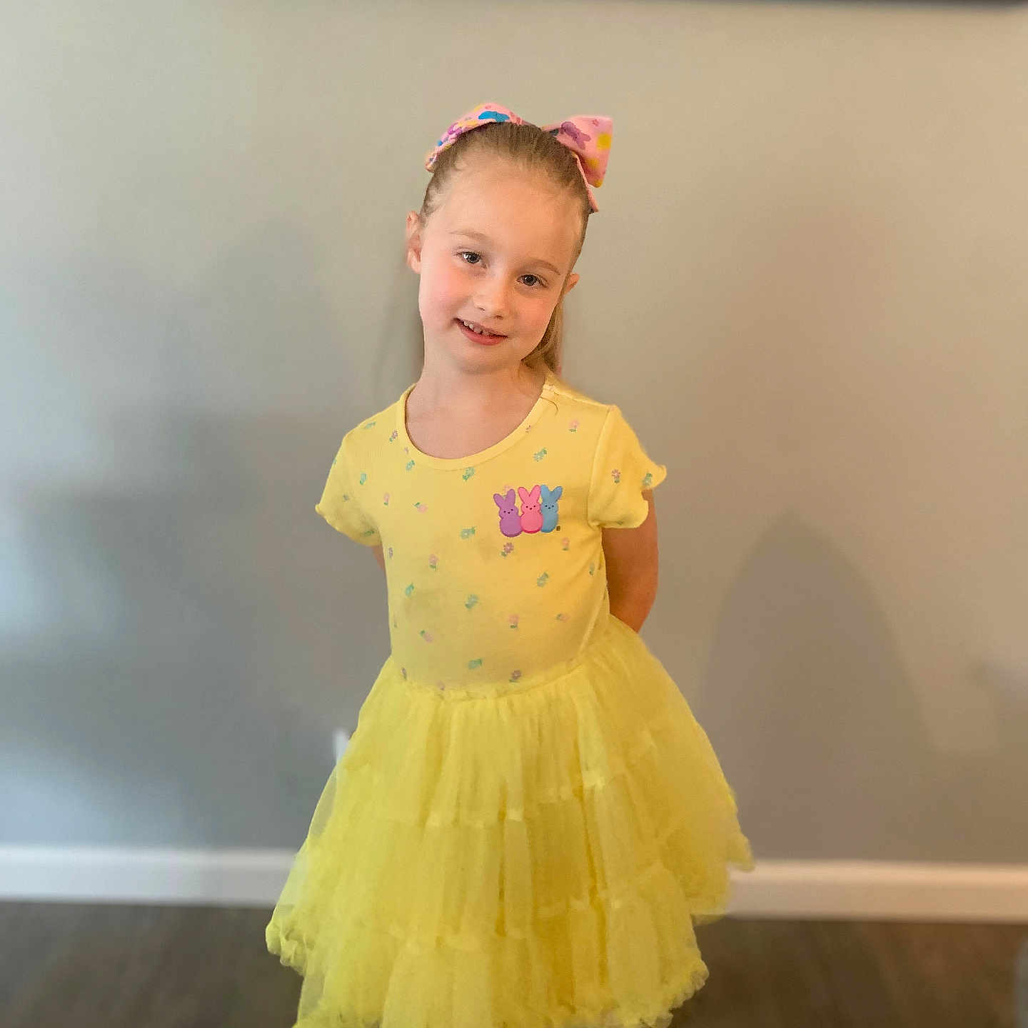 Venus is registered to the contest to win money with this photo: child, girl, yellow_dress, bow, smile, pose, indoor, floor, wall, painting, happy, person, fashion, colorful, cute, portrait, standing, toddler, hair, clothing