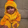 baby, child, costume, duck, yellow, hood, couch, smile, cute, indoors, feet, hand, plush, sitting, face, person, apparel, cozy, infant, happy