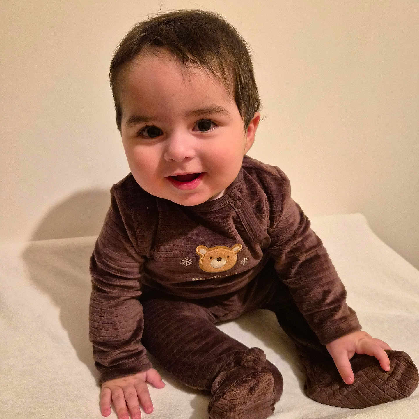 Ilyan a rejoint le concours — aidez-le/la à gagner de superbes lots ! baby, bear_emblem, brown_outfit, child, clothing, cozy, cute, cute_expression, face, feet, hands, happy, indoor, infant, person, portrait, sitting, smiling, warm_tone, young_child