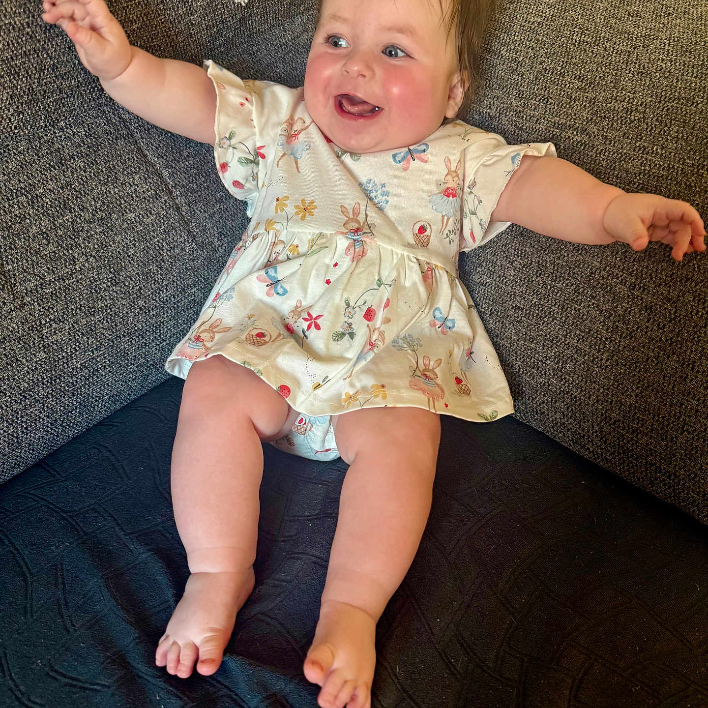 Daisy is registered to the contest to win money with this photo: arms_outstretched, baby, barefoot, bunny_pattern, child, clothing, couch, cute, dress, furniture, happy, home, indoor, infant, person, plush, portrait, rosy_cheeks, seated, smiling