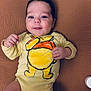 Timéo participe au concours pour gagner de l'argent avec cette photo : baby, infant, child, onesie, yellow_clothing, cartoon_print, smile, face, eyes, hand, blanket, brown_background, lying_down, cute, soft_light, portrait, indoors, skin, young_child, happy