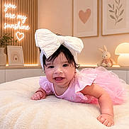 Kaylani joined the competition — help win amazing prizes! baby, child, infant, smiling, crawling, pink_dress, large_bow, headband, nursery, bed, blanket, stuffed_bunny, lamp, wall_art, heart, indoor, portrait, happy, decor, warm_lighting