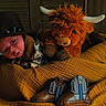 baby, infant, cowboy_hat, plush_toy, highland_cow, stuffed_animal, blanket, boots, portrait, indoors, cozy, sleeping_area, baby_clothing, cowboy_theme, orange, mustard, rustic, cute, face, photography