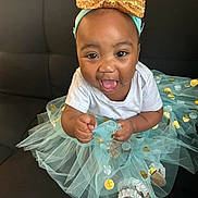 Kalani joined the competition — help win amazing prizes! baby, child, tutu, headband, golden_bow, blue_tutu, polka_dots, smiling, happy, sitting, black_couch, white_shirt, sandals, cute, indoors, portrait, toddler, fashion, playful, face