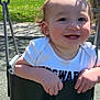 toddler, child, swing, playground, park, smiling, outdoor, daylight, white_shirt, camouflage_pants, happy, baby_teeth, rosy_cheeks, metal_chains, shadow, green_grass, trees, pavilion, person, fun