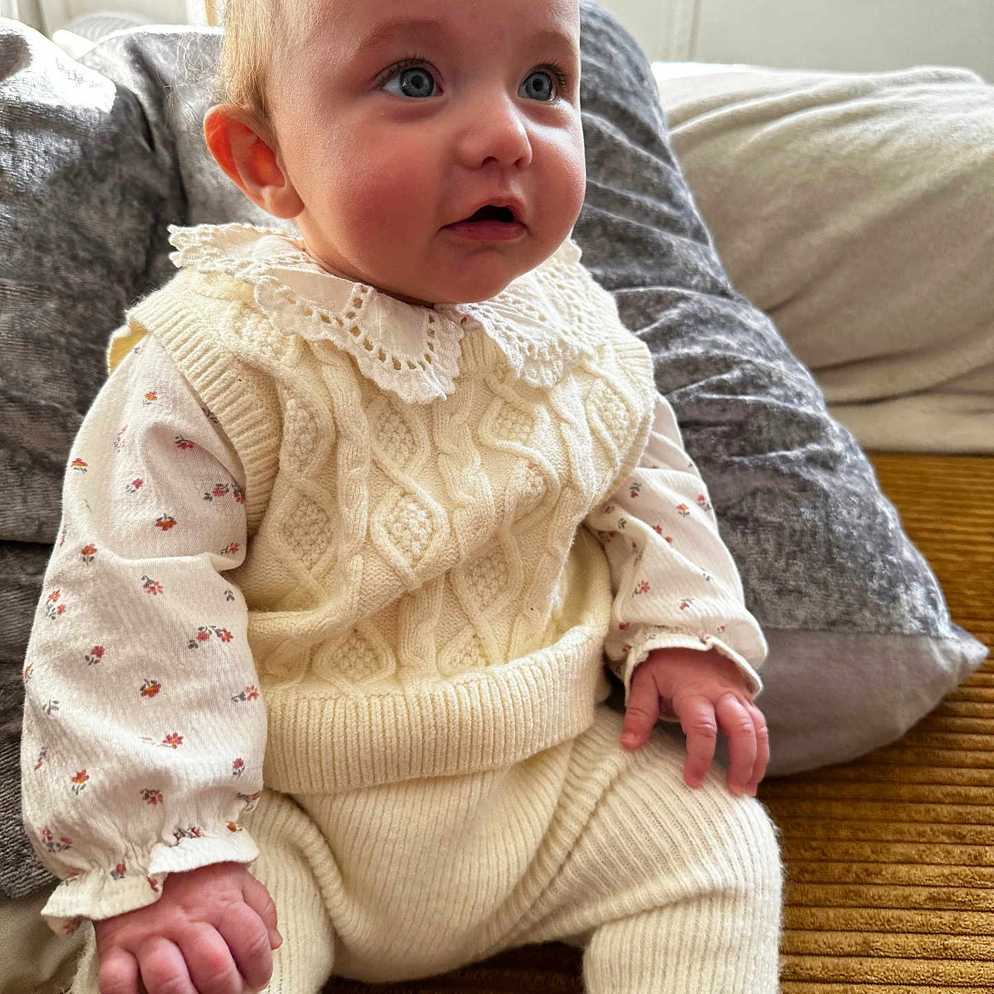 Talia a rejoint le concours — aidez-le/la à gagner de superbes lots ! baby, blanket, blue_eyes, child, close_up, couch, curly_hair, cute, fair_skin, floral_onesie, hands, indoor, infant, knit_sweater, lace_collar, pillow, plush_texture, portrait, sitting, soft_lighting