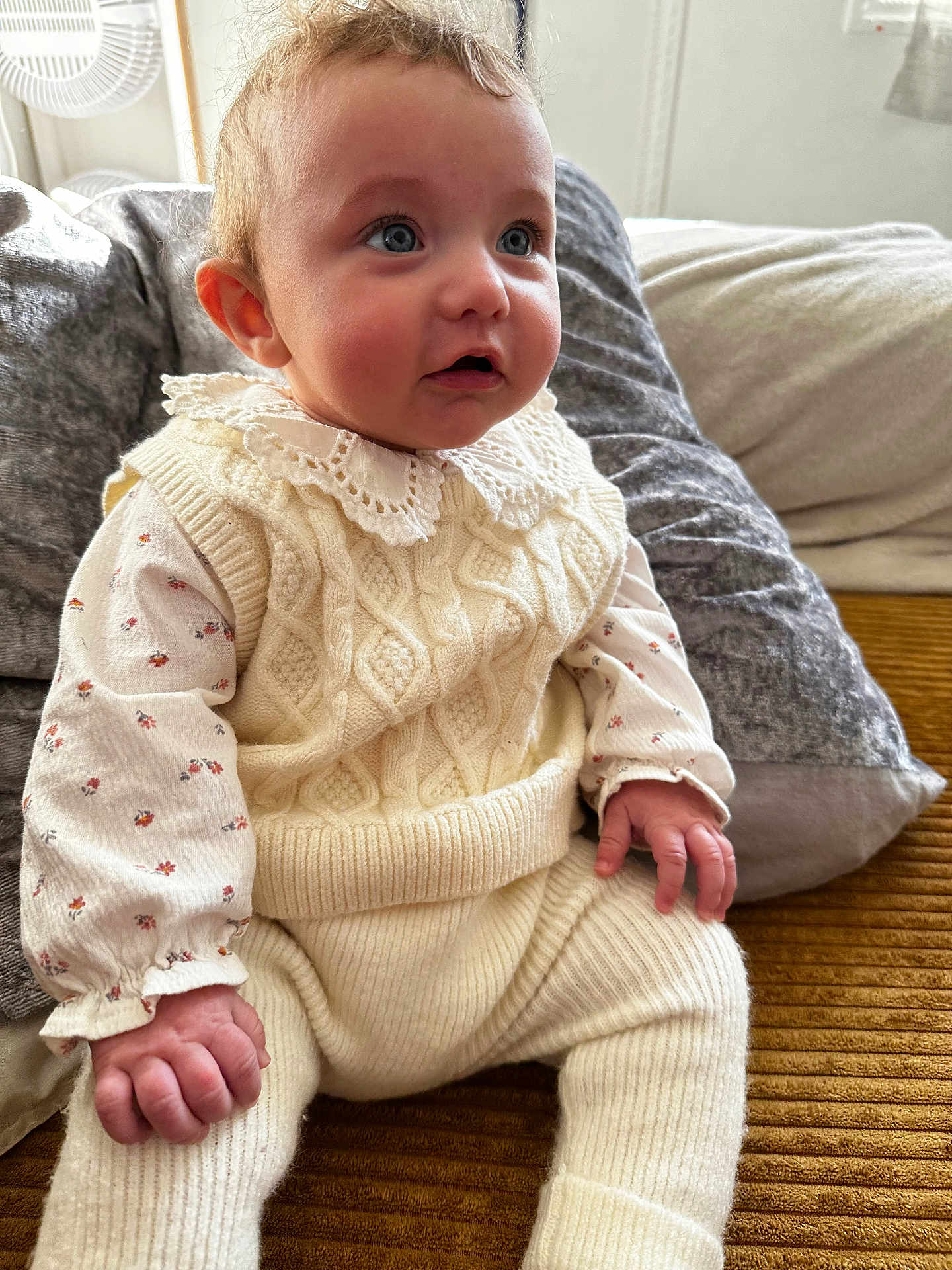 Talia a rejoint le concours — aidez-le/la à gagner de superbes lots ! baby, infant, child, knit_sweater, lace_collar, floral_onesie, blue_eyes, hands, cute, sitting, couch, pillow, blanket, indoor, portrait, soft_lighting, fair_skin, plush_texture, curly_hair, close_up
