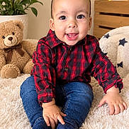 Aarón is registered to the contest to win money with this photo: baby, child, infant, sitting, smiling, happy, portrait, indoor, plaid_shirt, red_shirt, jeans, blue_pants, socks, rug, teddy_bear, plants, furniture, cushion, cozy, photography
