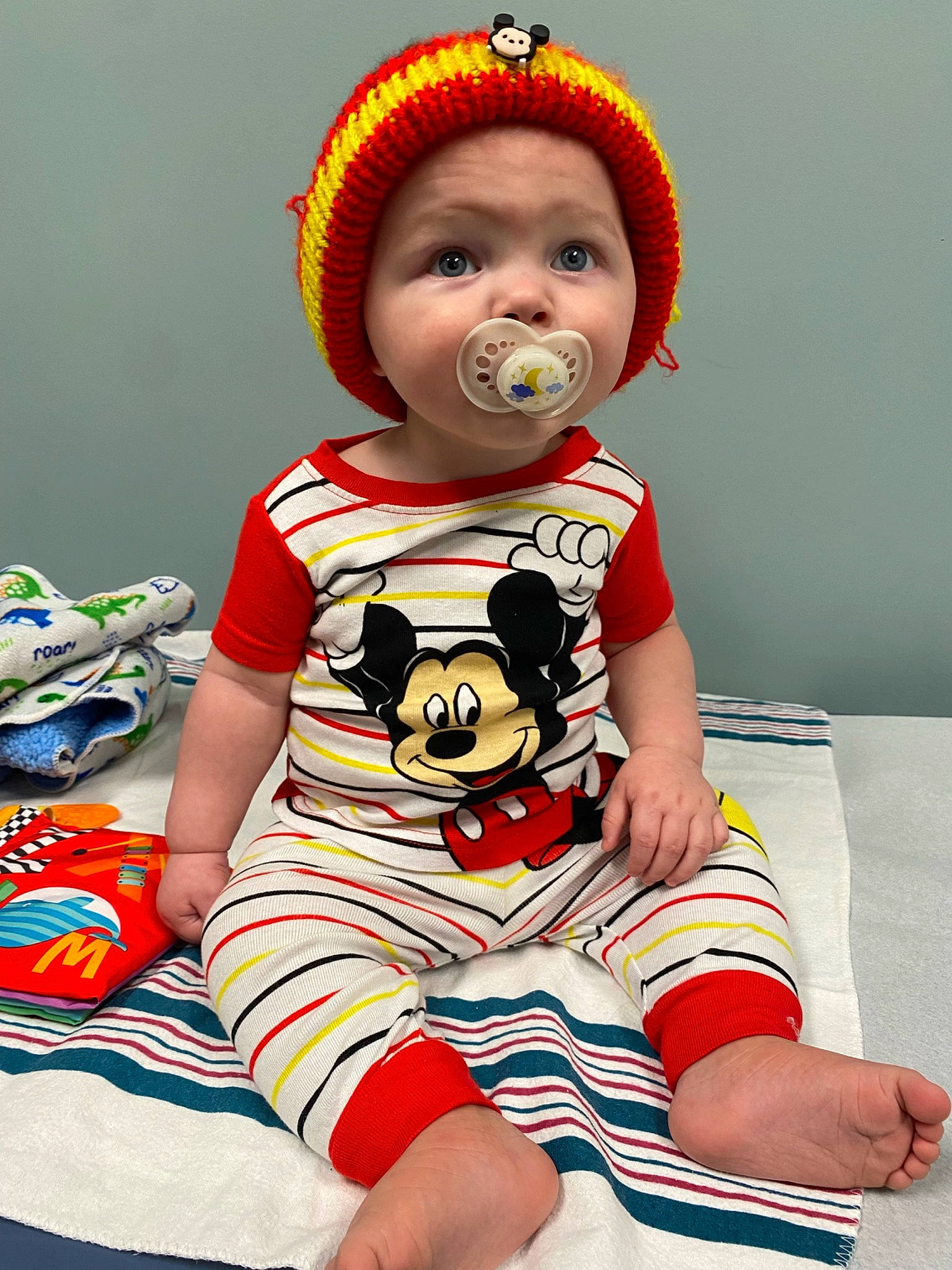 Greyson is registered to the contest to win money with this photo: baby, baby_toddler_clothing, cap, carmine, child, costume_hat, elbow, facial_expression, fun, happy, headwear, human_leg, knee, pattern, person, red, sitting, sleeve, t_shirt, thigh