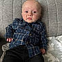 baby, black_pants, blanket, blue_shirt, casual, child, clothing, couch, expression, face, home, indoor, infant, looking_at_camera, person, plaid_shirt, portrait, seated, soft_lighting, young_child