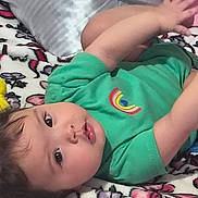 Starlyn is registered to the contest to win money with this photo: baby, child, infant, portrait, lying_down, bed, bedspread, pillow, plush_toy, green_shirt, yellow_toy, brown_hair, face, eyes, smiling, indoor, home, colorful, casual, photography
