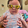 Starlyn joined the competition — help win amazing prizes! baby, child, infant, portrait, sunglasses, reflective_glasses, floral_shirt, blue_jeans, held_baby, adult_hands, indoor, home, furniture, seated, close_up, face, serious_expression, photographer_reflection, colorful_clothing, family