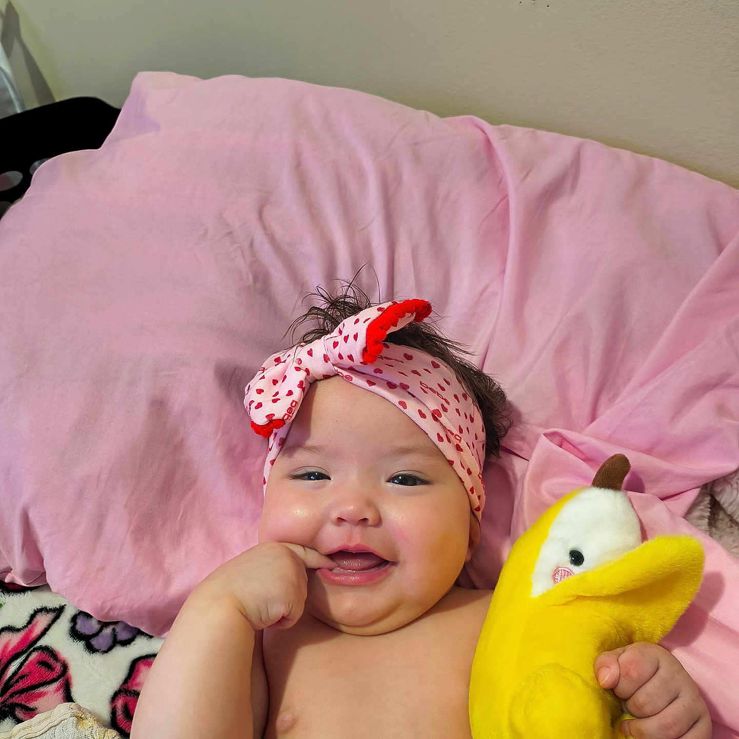 Starlyn joined the competition — help win amazing prizes! baby, infant, child, smiling, happy, portrait, indoors, bed, pillow, pink, headband, plush_toy, duck, toy, lying_down, bare_chested, hand, finger, blanket, bedroom