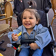 Elia-Maria a rejoint le concours — aidez-le/la à gagner de superbes lots ! toddler, stroller, smile, lemon, pony_tail, denim_jacket, jeans, outdoor, cafe, chair, wicker_chair, child, happy, person, seat_belt, toy, playful, daylight, casual_clothing, cute