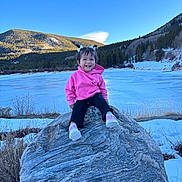 Isabella joined the competition — help win amazing prizes! blue_sky, casual_clothing, child, daytime, footwear, frozen_lake, happy, landscape, mountain, nature, outdoor, person, pigtails, pink_hoodie, rock, smiling, snow, toddler, trees, winter