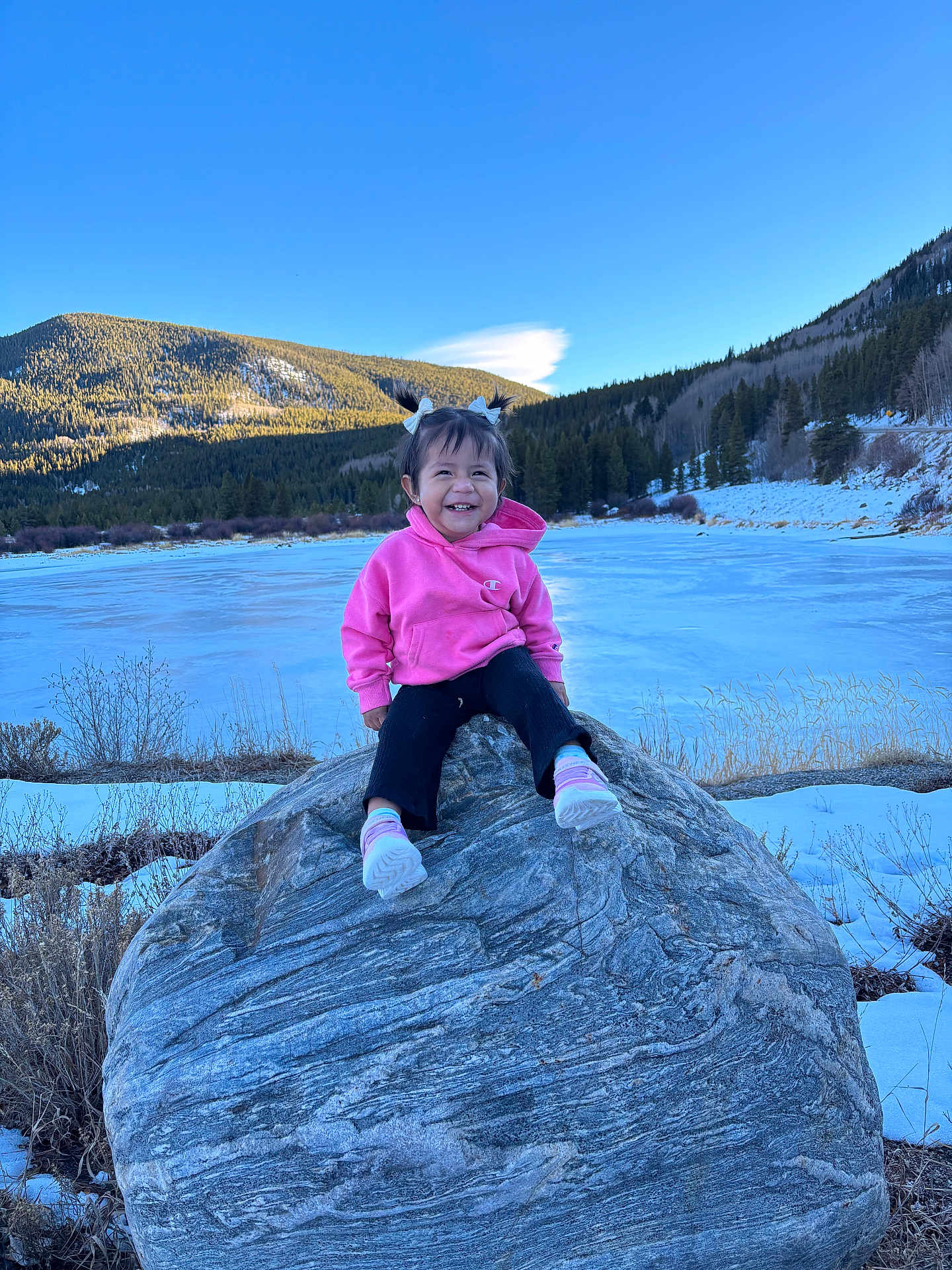Isabella joined the competition — help win amazing prizes! blue_sky, casual_clothing, child, daytime, footwear, frozen_lake, happy, landscape, mountain, nature, outdoor, person, pigtails, pink_hoodie, rock, smiling, snow, toddler, trees, winter