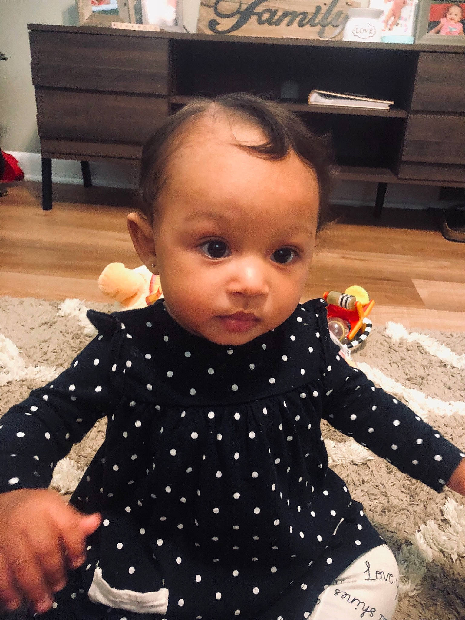 Raeleigh is registered to the contest to win money with this photo: baby, baby_toddler_clothing, cheek, child, dress, eye, facial_expression, floor, flooring, fun, gesture, hand, happy, pattern, person, sitting, skin, sleeve, standing, thumb