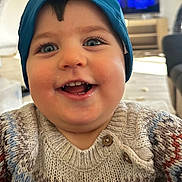 Iman participe au concours pour gagner de l'argent avec cette photo : toddler, child, smile, happy, blue_eyes, hood, sweater, knitted, face, indoor, living_room, person, cute, portrait, baby, close_up, cozy, warm_clothing, cheerful, young_child