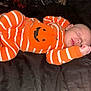 baby, sleeping, infant, onesie, orange, white_stripes, jack_o_lantern, cozy, blanket, bed, resting, cute, child, newborn, person, face, hand, mouth, nose, ear