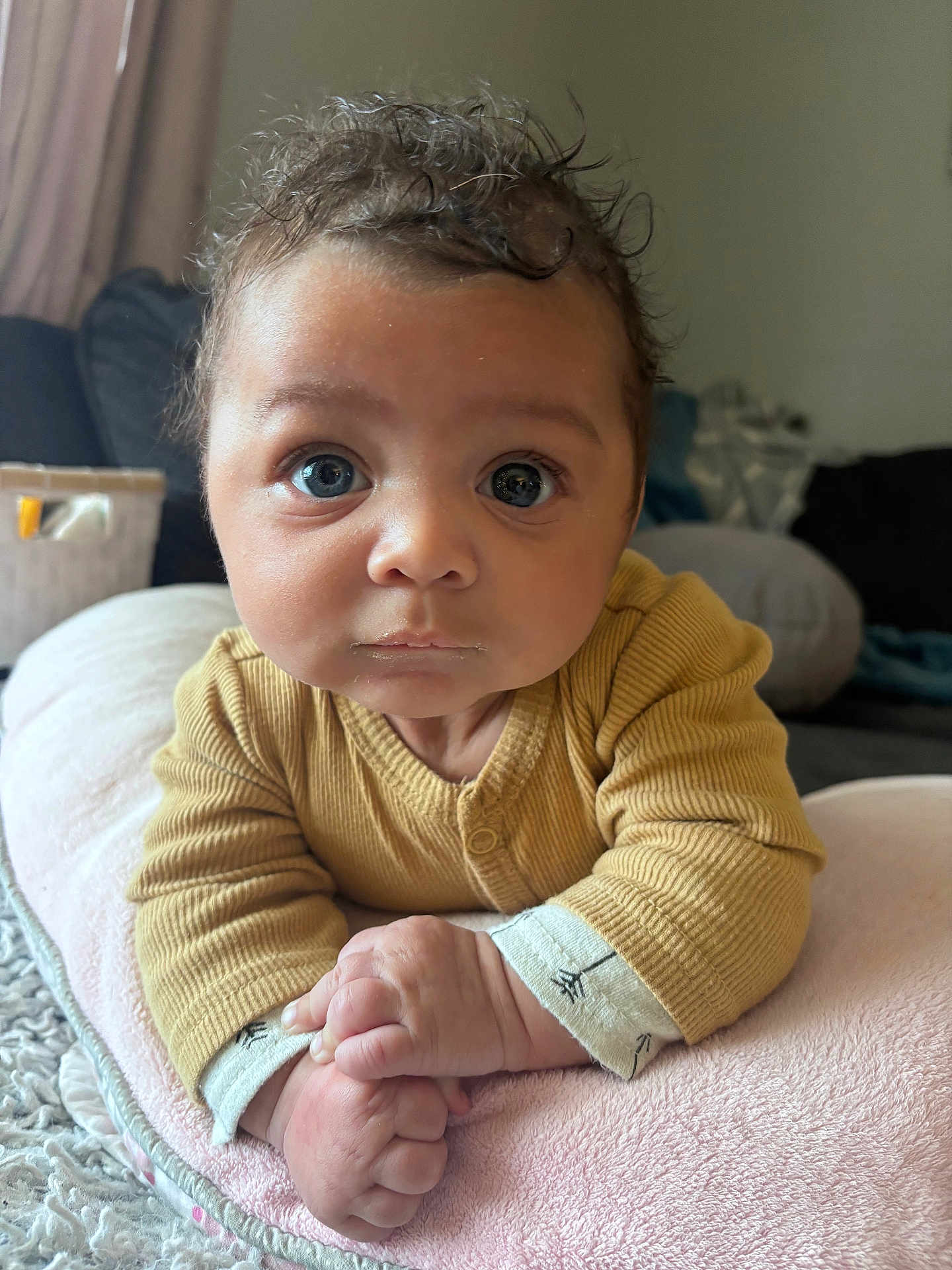 Roman joined the competition — help win amazing prizes! baby, infant, child, face, curly_hair, big_eyes, yellow_clothing, pillow, soft_texture, hands, indoors, couch, blanket, closeup, portrait, cute, expression, curious, resting, cozy