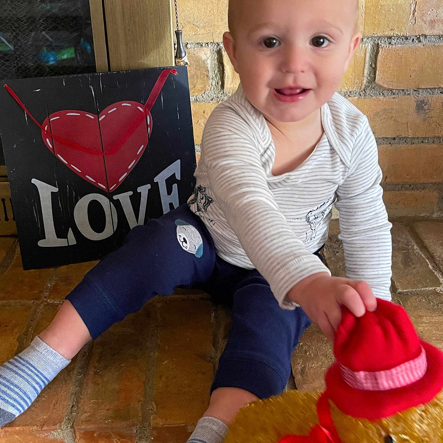Louis joined the competition — help win amazing prizes! baby, blue_pants, brick_floor, child, cute, decor, floor, happy, indoor, love_sign, person, playful, portrait, red_hat, red_scarf, smiling, socks, striped_shirt, teddy_bear, toy