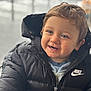 toddler, child, smiling, blue_eyes, black_jacket, nike_logo, puffer_jacket, curly_hair, portrait, indoor, warm_clothing, cute, happy, face, person, young_child, casual_wear, close_up, baby, winter_clothes