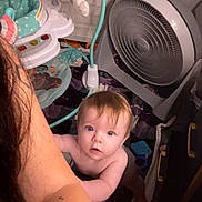 Lorelai is registered to the contest to win money with this photo: arm, baby, baby_gear, blanket, blue_eyes, child, curious, fan, floor, hair, holding, household_item, indoor, light, looking_up, person, room, skin, tattoo, toy