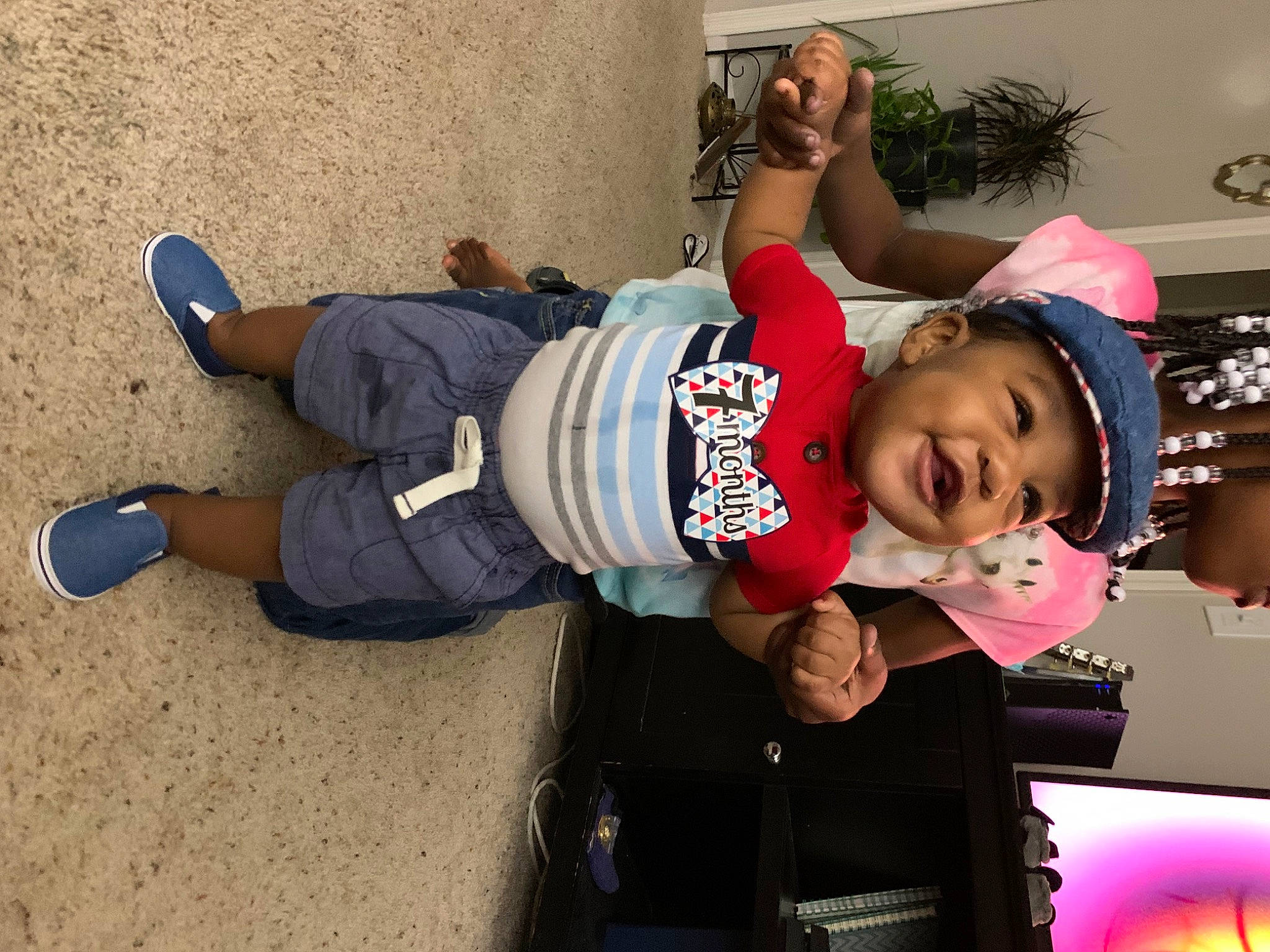 Michael Jr is registered to the contest to win money with this photo: baby, baseball_cap, cap, child, costume, event, fun, happy, hat, headwear, houseplant, human_leg, knee, leisure, person, plant, recreation, sneakers, t_shirt, thigh