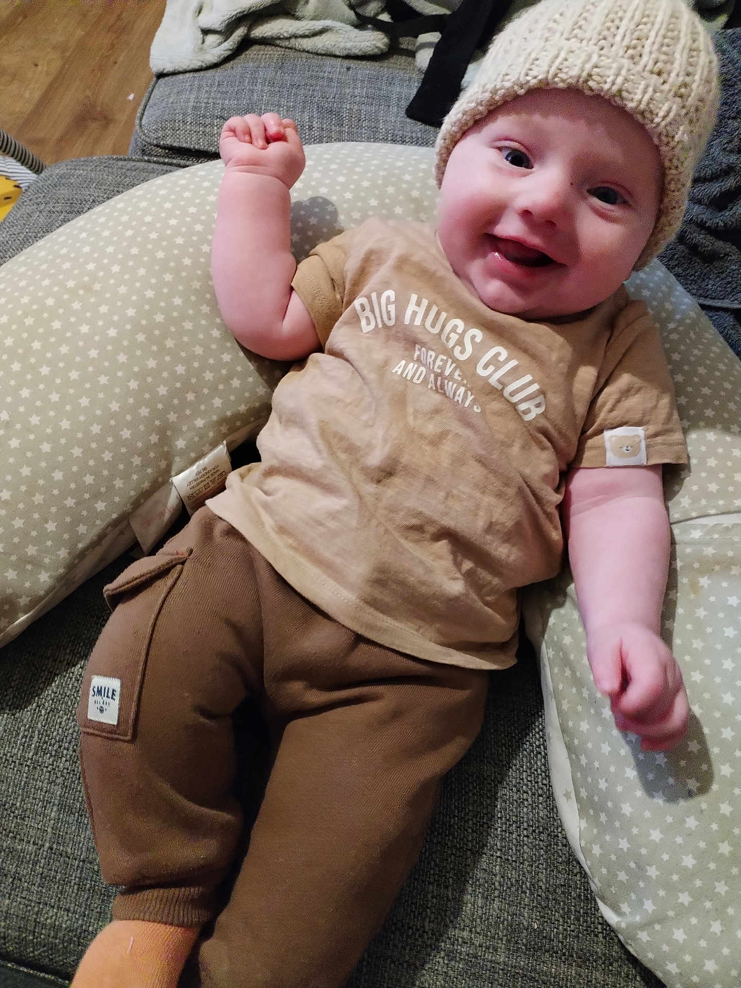 Reginald is registered to the contest to win money with this photo: arm, baby, casual_clothing, child, couch, cozy, face, happy, hat, indoor, infant, knitted, pants, pillow, portrait, relaxed, smiling, socks, star_pattern, tshirt