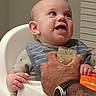 Carson joined the competition — help win amazing prizes! baby, high_chair, feeding, adult_hand, watch, tattoo, food_jar, spoon, smiling, indoor, clothing, bib, person, child, mealtime, happy, face, portrait, home, furniture