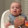 baby, bib, child, clothing, cup, curious, expression, face, feeding, food, hand, high_chair, indoor, meal, parent, person, sitting, table, tattoo, watch
