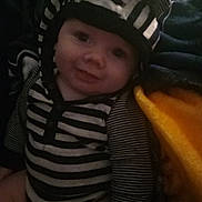Kaycen joined the competition — help win amazing prizes! baby, blanket, child, cozy, cute, ears, face, hat, indoors, infant, orange_blanket, person, portrait, sitting, smile, soft_lighting, striped_clothing, striped_hat, striped_shirt, young_child