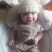 Kaycen is registered to the contest to win money with this photo: baby, smiling, hat, knitted, bear_ears, overalls, beige_clothing, white_shirt, baby_seat, cushion, happy, infant, cute, child, small_hands, indoor, portrait, person, clothing, headwear