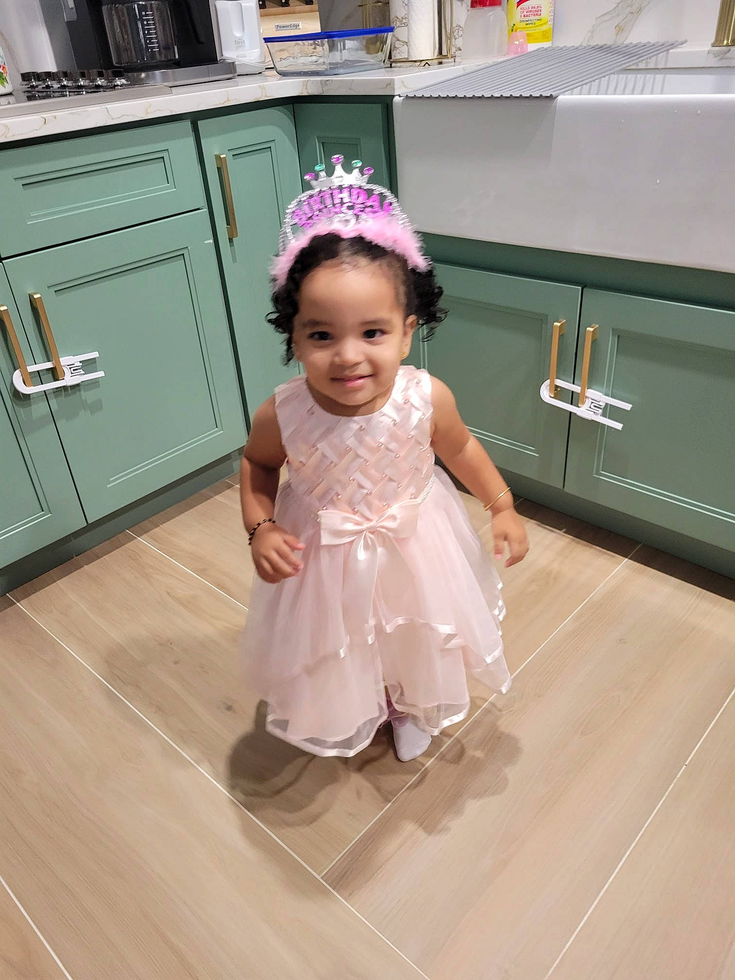Nafiza is registered to the contest to win money with this photo: baby, baby_toddler_clothing, cabinetry, child, door, dress, event, fashion_accessory, floor, flooring, happy, hardwood, headpiece, human_leg, joy, person, shelf, skin, smile, standing