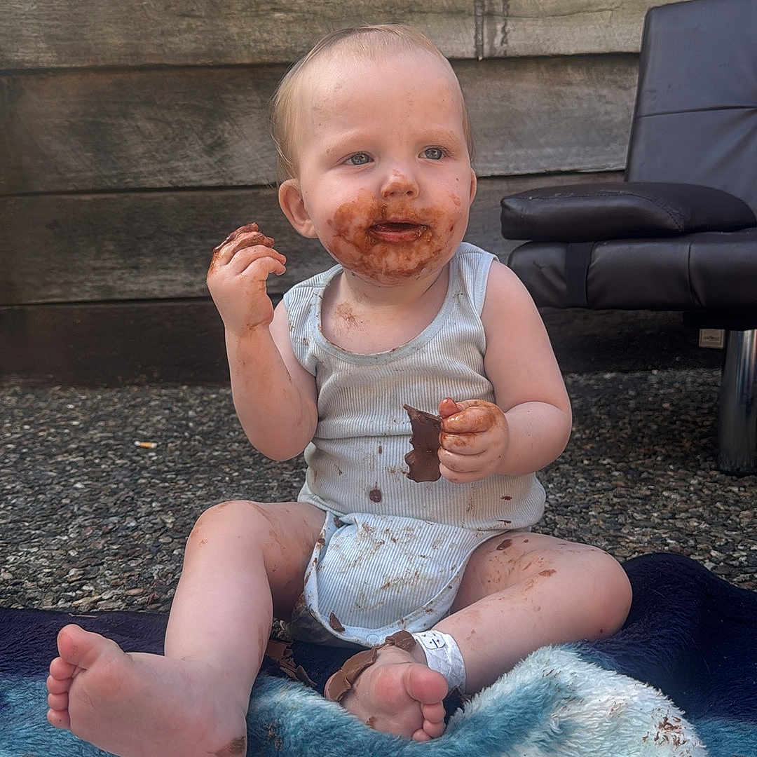 Archie-Alexander is registered to the contest to win money with this photo: baby, bodypart, clothing, cream, cutlery, dessert, face, finger, food, furniture, hand, head, icecream, pants, person, photography, portrait, shorts, sitting, summer