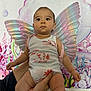 baby, child, infant, fairy_wings, onesie, underwater_theme, colorful, background, hands, face, cute, curious, indoor, person, holding, fish_print, shells, coral, pink, decor