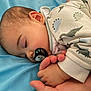 baby, sleeping, pacifier, hand, pajamas, dinosaur_pattern, blue_blanket, infant, cozy, peaceful, child, cute, soft, rest, closeup, skin, face, ear, fingers, comfort