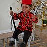 Jaden is registered to the contest to win money with this photo: toddler, child, traditional_clothing, red_hat, walking_stick, chair, carpet, indoor, television, cartoon, happy, smiling, home_decor, plant, golden_shelf, ornaments, black_pants, socks, candid, portrait