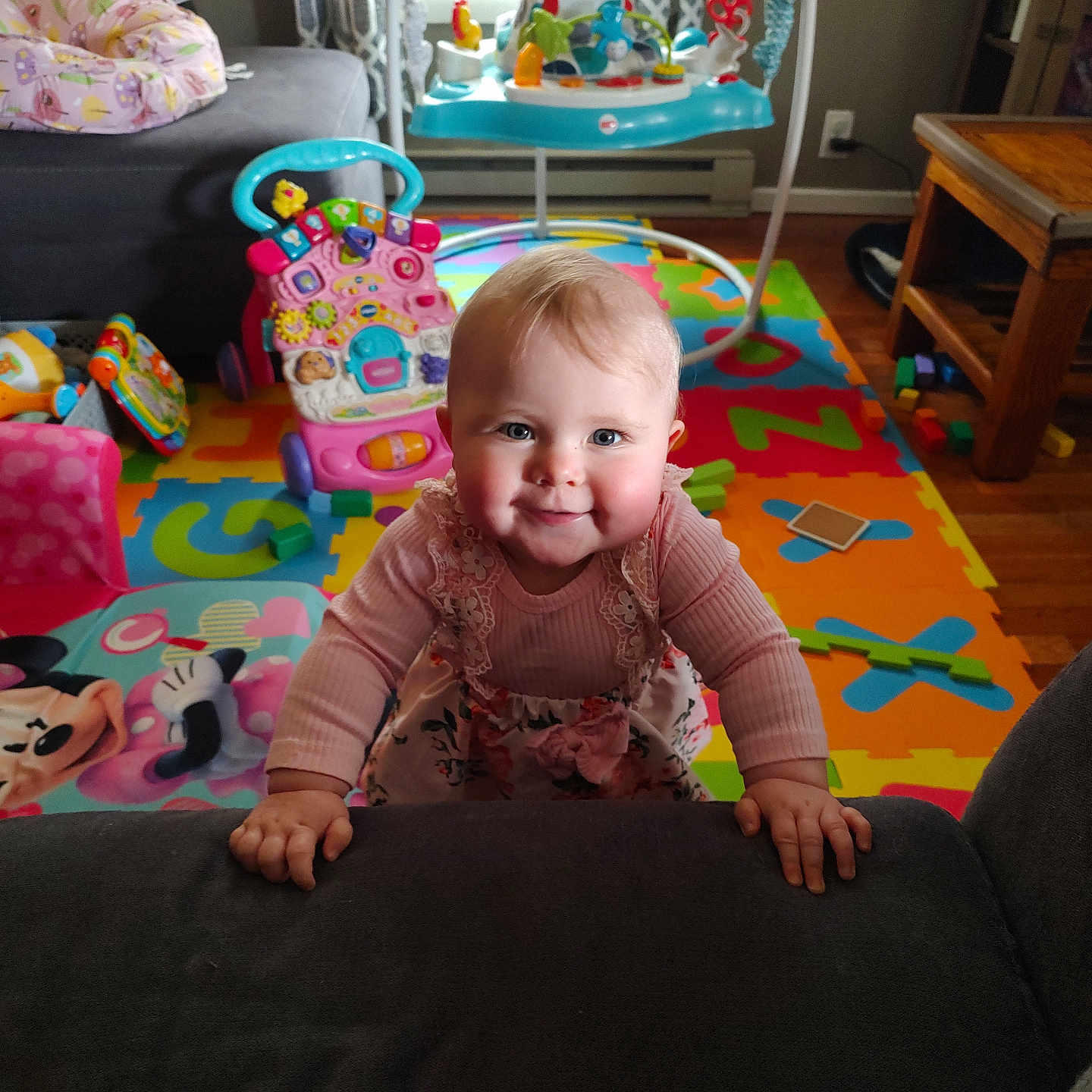 Adalee is registered to the contest to win money with this photo: baby, chair, child, colorful, couch, cute, floor_mat, happy, indoor, minnie_mouse, mischievous, person, pink_clothing, plastic_toy, playroom, smiling, table, toys, wooden_floor, young_child