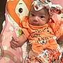 baby, infant, girl, headband, bow, orange_clothing, floral_pattern, baby_seat, polka_dots, cartoon_animals, hearts, cute, portrait, indoor, child, smiling, expression, person, young_child, colorful