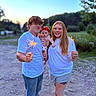 baby, child, couple, sparklers, outdoor, evening, nature, smiling, family, casual_clothing, redhead, jeans, shorts, grass, trees, dirt_road, portrait, happy, people, summer