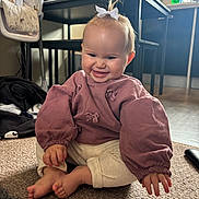 Isla is registered to the contest to win money with this photo: baby, barefoot, bow, cabinets, carpet, child, hair_bow, happy, high_chair, household, indoor, infant, kitchen, long_sleeves, pink_clothing, playpen, portrait, sitting, smiling, white_pants