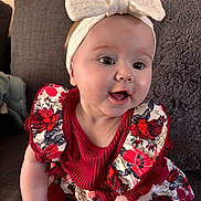 Isla is registered to the contest to win money with this photo: baby, child, smiling, headband, bow, dress, floral_pattern, couch, pillow, indoor, happy, cute, person, portrait, infant, young_child, sitting, skin, face, apparel