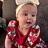 baby, child, smiling, headband, bow, dress, floral_pattern, couch, pillow, indoor, happy, cute, person, portrait, infant, young_child, sitting, skin, face, apparel