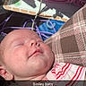 baby, smile, sleeping, face, infant, striped_clothing, strawberry_patch, blanket, plaid_pattern, soft_light, child, peaceful, cute, indoors, newborn, head, hand, resting, cozy, portrait