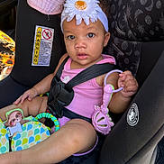 Kollyns is registered to the contest to win money with this photo: baby_toy, car_interior, car_seat, child, colorful, curly_hair, cute, cute_expression, flower, headband, indoor, infant, pink_clothing, playful, safety, seatbelt, sitting, toddler, toy, young_child