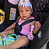 baby_toy, car_interior, car_seat, child, colorful, curly_hair, cute, cute_expression, flower, headband, indoor, infant, pink_clothing, playful, safety, seatbelt, sitting, toddler, toy, young_child