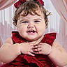baby, child, dress, red_dress, bows, curly_hair, smile, happy, portrait, hands, cute, indoors, curtains, pink_curtains, toddler, face, chubby_cheeks, cute_expression, person, young_child
