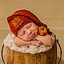 baby, sleeping, orange_hat, knit_hat, pumpkin_patch, felt_pumpkin, wooden_bucket, fluffy_blanket, resting, cute, infant, portrait, cozy, soft_texture, newborn, peaceful, child, indoors, warm_colors, adorable