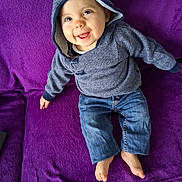 Lylio participe au concours pour gagner de l'argent avec cette photo : baby, barefoot, casual_wear, cheerful, child, clothing, cozy_clothing, cute, denim_pants, face, happy, hoodie, indoor, infant, person, portrait, purple_blanket, sitting, smiling, young_child